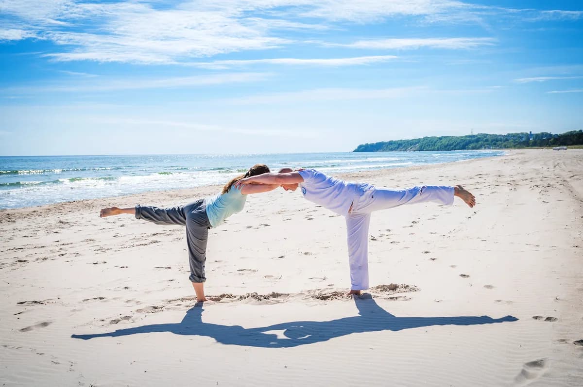 Zwei Menschen bei einer Yoga-Balanceübung am Ostseestrand